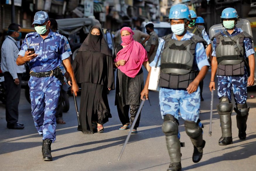 Veiled Muslim women walk past members of Rapid Action Force (RAF) patrolling a neighborhood during a lockdown in the area after dozens of men were taken to a quarantine facility amid concerns about the spread of coronavirus disease (COVID-19)