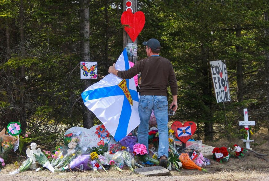 A man adjusts the Nova Scotia flag in front of the makeshift memorial, made in the memory for the victims of Sunday’s mass shooting in Portapique, Nova Scotia, Canada April 23, 2020. REUTERS/Tim Krochak