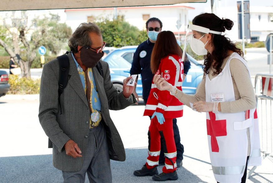 A Red Cross volunteer checks temperature of a customer at the entrance of an open-air food market that has been reopened, during the coronavirus disease (COVID-19) outbreak in Cisternino, Italy, April 27, 2020. REUTERS/Alessandro Garofalo