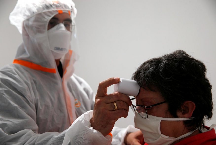 A French doctor wearing a protective suit checks the temperature of a woman in a testing site for the coronavirus disease (COVID-19) in Gouzeaucourt, France, April 28, 2020. REUTERS/Pascal Rossignol
