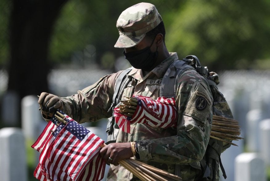 A U.S. Army Old Guard member holds small American flags to put in front of the headstones of U.S. service members buried at Arlington National Cemetery in Arlington, Virginia, U.S., May 21, 2020. REUTERS/Tom Brenner