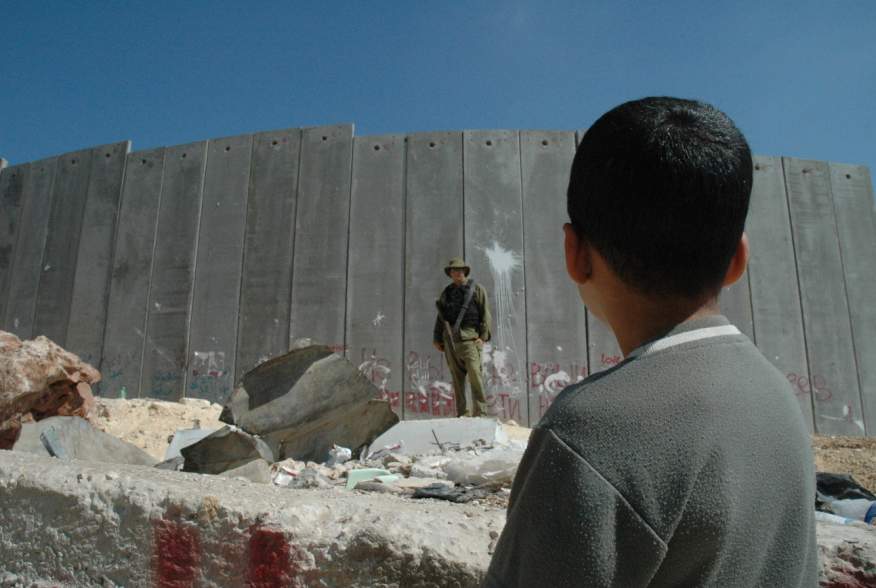 English: A Palestinian boy and Israeli soldier in front of the Israeli West Bank Barrier.