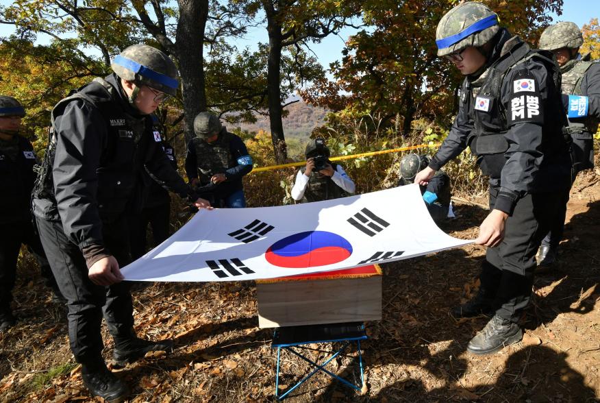 Members of South Korea's Defence Ministry recovery team cover a casket containing a piece of bone believed to be the remains of an unidentified South Korean soldier killed in the Korean War with the national flag in the Demilitarized Zone (DMZ) dividing t