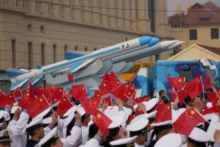 Chinese People's Liberation Army (PLA) Navy soldiers wave Chinese flags next to a model of a military vehicle carrying anti-ship missiles, during an event marking the 70th anniversary of the founding of Chinese People's Liberation Army Navy on April 23