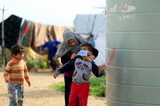 A Syrian refugee woman puts a face mask on a boy as a precaution against the spread of coronavirus, in al-Wazzani area, in southern Lebanon, March 14, 2020. REUTERS/Ali Hashisho