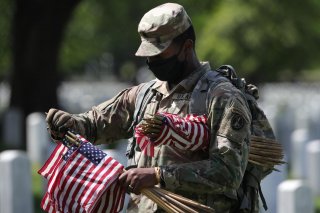 A U.S. Army Old Guard member holds small American flags to put in front of the headstones of U.S. service members buried at Arlington National Cemetery in Arlington, Virginia, U.S., May 21, 2020. REUTERS/Tom Brenner