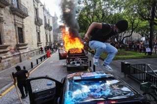 A demonstrator jumps on a damaged police vehicle after demonstrators set it on fire during a protest to demand justice for Giovanni Lopez, a construction worker who died after being arrested for not wearing a face mask in public, during the coronavirus di