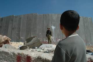 English: A Palestinian boy and Israeli soldier in front of the Israeli West Bank Barrier.