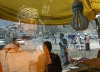 A shopkeeper stands inside a shop as people are reflected on a window panel in Kabul April 8, 2012. REUTERS/Omar Sobhani
