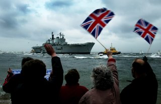 People wave as the flagship of Britain's Royal Navy HMS (Her Majesty's Ship) Ark Royal approaches Portsmouth Harbour on the coast of southern England, after operations in the Gulf conflict, May 17, 2003. REUTERS/Michael Crabtree