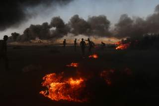 Palestinian demonstrators are seen as smoke rises from burning tires during a protest marking the 70th anniversary of Nakba, at the Israel-Gaza border in the southern Gaza Strip May 15, 2018. REUTERS/Ibraheem Abu Mustafa