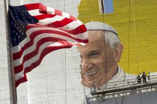 The U.S. flag flies as painters work on a mural of Pope Francis on the side of a building in midtown Manhattan in New York August 28, 2015. Pope Francis is scheduled to visit Washington D.C., New York and Philadelphia September 22-27.