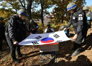 Members of South Korea's Defence Ministry recovery team cover a casket containing a piece of bone believed to be the remains of an unidentified South Korean soldier killed in the Korean War with the national flag in the Demilitarized Zone (DMZ) dividing t