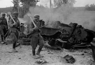 Finnish soldiers carrying Panzerfäuste on their shoulders pass by the remains of a destroyed Soviet T-34 tank at the Battle of Tali-Ihantala