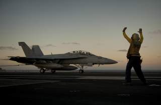 U.S. Navy Aviation Boatswain's Mate 3rd Class Tilford Breedlove signals to the pilot of an F/A-18F Super Hornet aircraft, with the Strike Fighter Squadron 22, during an arrested landing on the flight deck of aircraft carrier USS Carl Vinson (CVN-70) in th