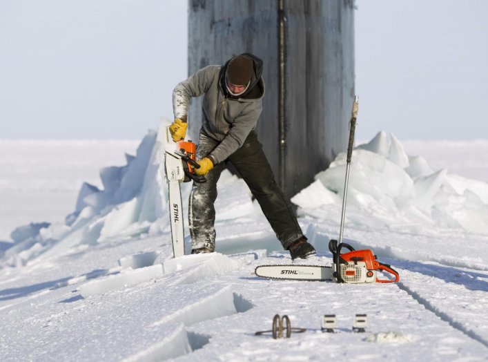 Applied Physics Laboratory Ice Station (APLS) employee Keith Magness uses a chainsaw to cut through ice on the hatches of the Seawolf class submarine USS Connecticut after the boat surfaced through Arctic sea ice during an exercise near the 2011 APLS camp