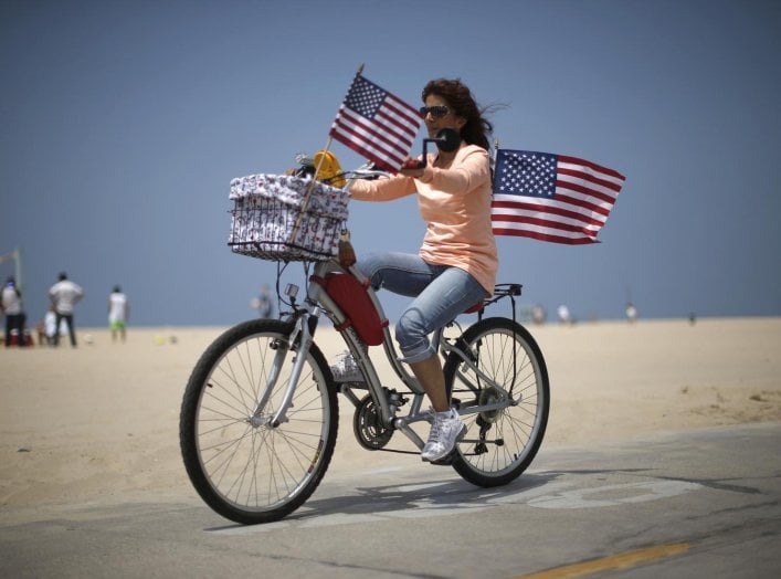A woman cycles with U.S. flags on Independence Day on Venice Beach in Los Angeles, California July 4, 2014. The holiday marks the signing of the Declaration of independence from the British on July 4, 1776. REUTERS/Lucy Nicholson