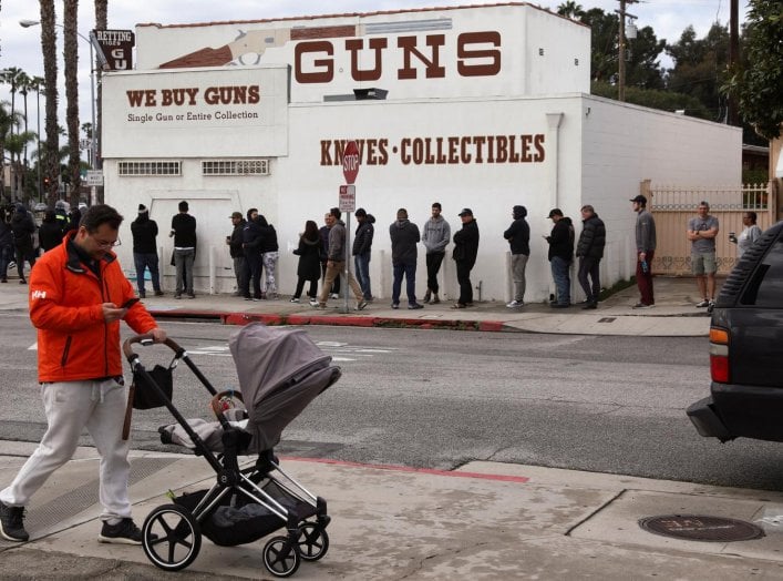 A pedestrian pushes a stroller as people wait in line outside to buy supplies at the Martin B. Retting, Inc. gun store amid fears of the global growth of coronavirus cases, in Culver City, California, U.S. March 15, 2020. REUTERS/Patrick T. Fallon