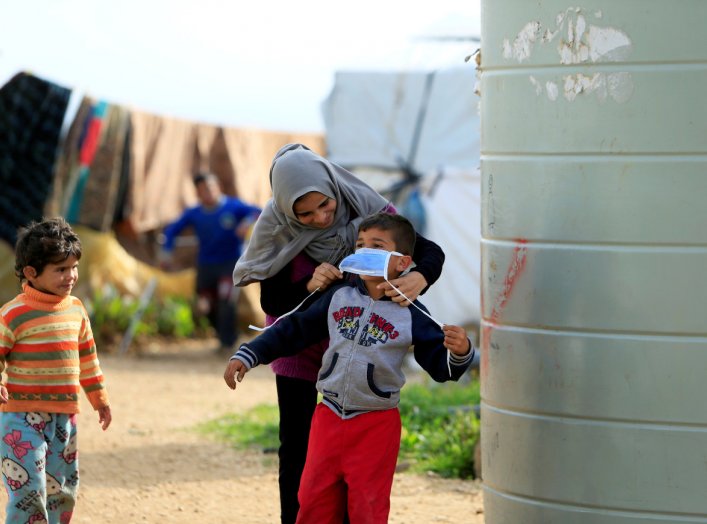 A Syrian refugee woman puts a face mask on a boy as a precaution against the spread of coronavirus, in al-Wazzani area, in southern Lebanon, March 14, 2020. REUTERS/Ali Hashisho