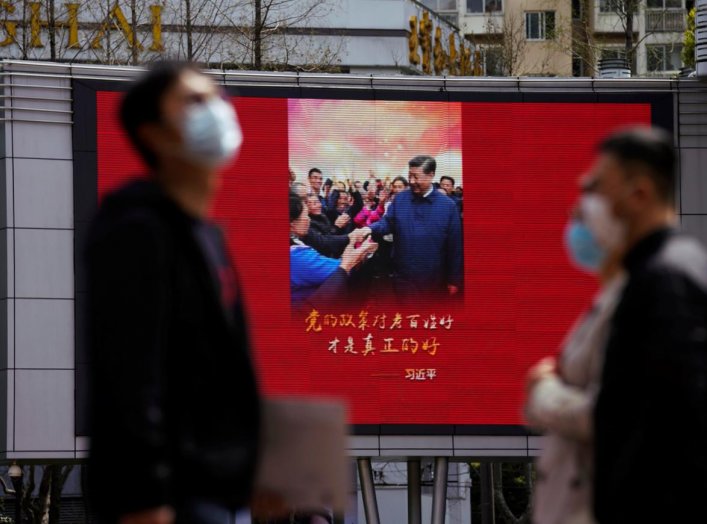 Pedestrians wearing face masks walk past a screen displaying an image of Chinese President Xi Jinping after the city's emergency alert level for coronavirus disease (COVID-19) was downgraded, in Shanghai, China March 23, 2020. REUTERS/Aly Song