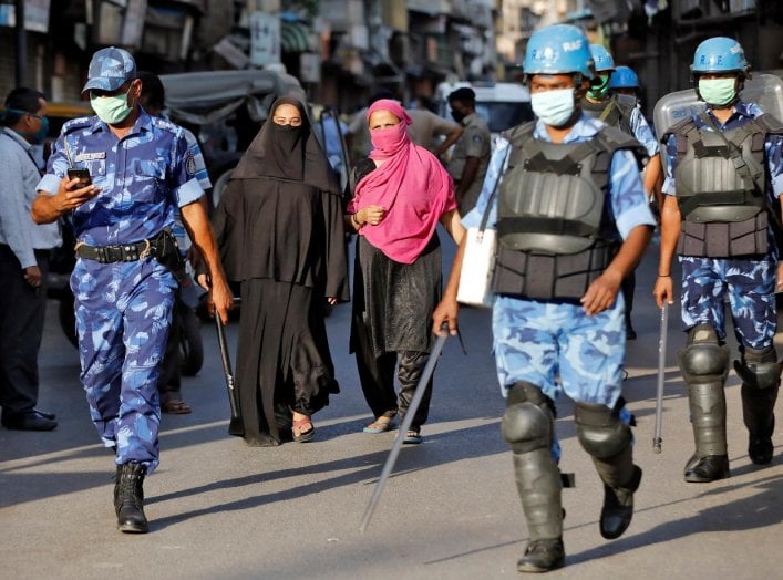 Veiled Muslim women walk past members of Rapid Action Force (RAF) patrolling a neighborhood during a lockdown in the area after dozens of men were taken to a quarantine facility amid concerns about the spread of coronavirus disease (COVID-19)