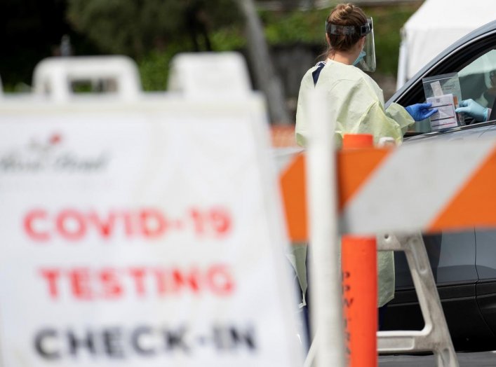 A health worker in protective gear hands out a self-testing kit in a parking lot of Rose Bowl Stadium during the global outbreak of the coronavirus disease (COVID-19), in Pasadena, California, U.S., April 8, 2020. REUTERS/Mario Anzuoni