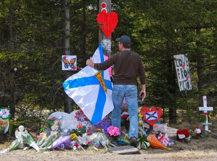 A man adjusts the Nova Scotia flag in front of the makeshift memorial, made in the memory for the victims of Sunday’s mass shooting in Portapique, Nova Scotia, Canada April 23, 2020. REUTERS/Tim Krochak