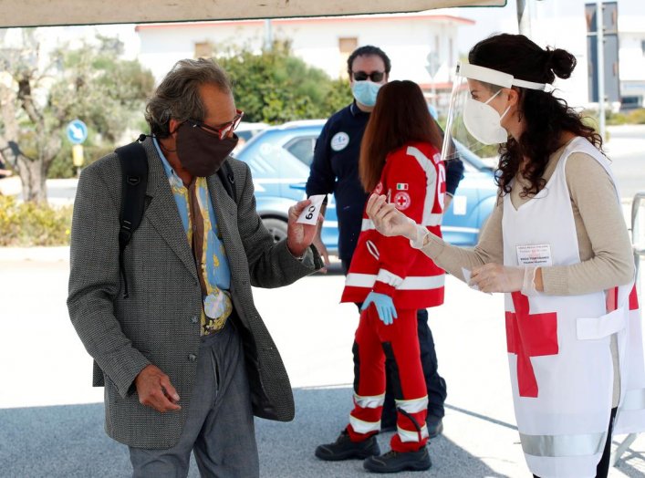 A Red Cross volunteer checks temperature of a customer at the entrance of an open-air food market that has been reopened, during the coronavirus disease (COVID-19) outbreak in Cisternino, Italy, April 27, 2020. REUTERS/Alessandro Garofalo