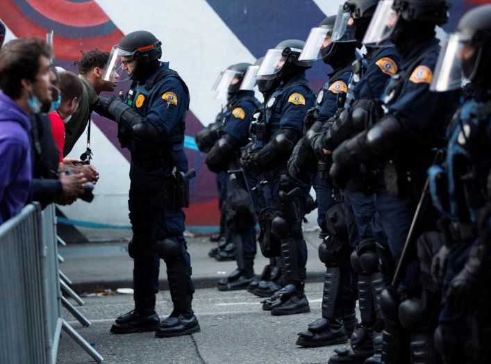 A line of Washington State Patrol officers in riot gear form as protesters point over a barricade during a protest against police brutality and the death in Minneapolis police custody of George Floyd, near Seattle Police Department's East Precinct in Seat