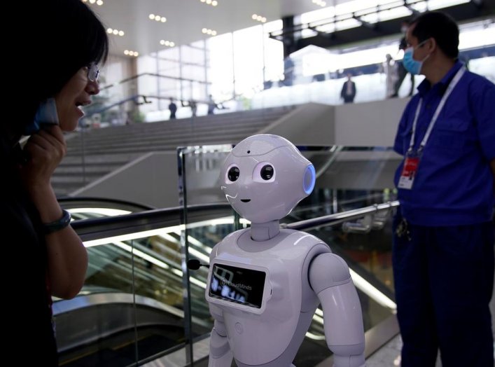 People wearing face masks following the coronavirus disease (COVID-19) outbreak are seen near a robot at the venue for the World Artificial Intelligence Conference (WAIC) in Shanghai, China July 9, 2020. REUTERS/Aly Song
