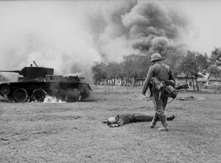German infantryman in front of fallen Russian tank soldier and burning BT-7 light tank in the southern Soviet Union during the early days of Operation Barbarossa