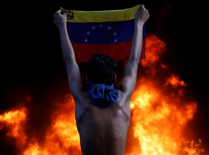 A protester holds a national flag as a bank branch, housed in the magistracy of the Supreme Court of Justice, burns during a rally against Venezuela's President Nicolas Maduro, in Caracas, Venezuela June 12, 2017. REUTERS/Carlos Garcia Rawlins TPX IMAGES 