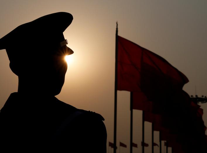 A paramilitary police officer is seen silhouetted in front of flags as he stands guard during the third plenary session of the Chinese People's Political Consultative Conference (CPPCC) in Beijing, China March 10, 2018.