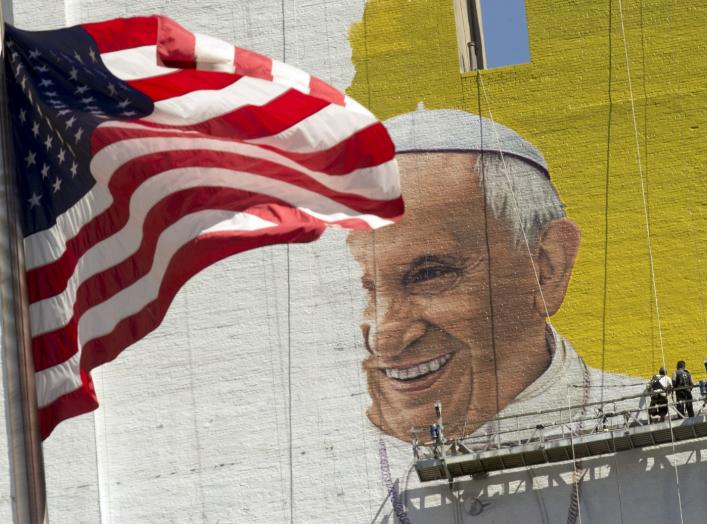 The U.S. flag flies as painters work on a mural of Pope Francis on the side of a building in midtown Manhattan in New York August 28, 2015. Pope Francis is scheduled to visit Washington D.C., New York and Philadelphia September 22-27.