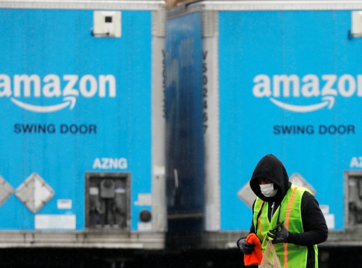 A worker in a face mask walks by trucks parked at an Amazon facility as the global coronavirus outbreak continued in Bethpage on Long Island in New York, U.S., March 17, 2020. REUTERS/Andrew Kelly