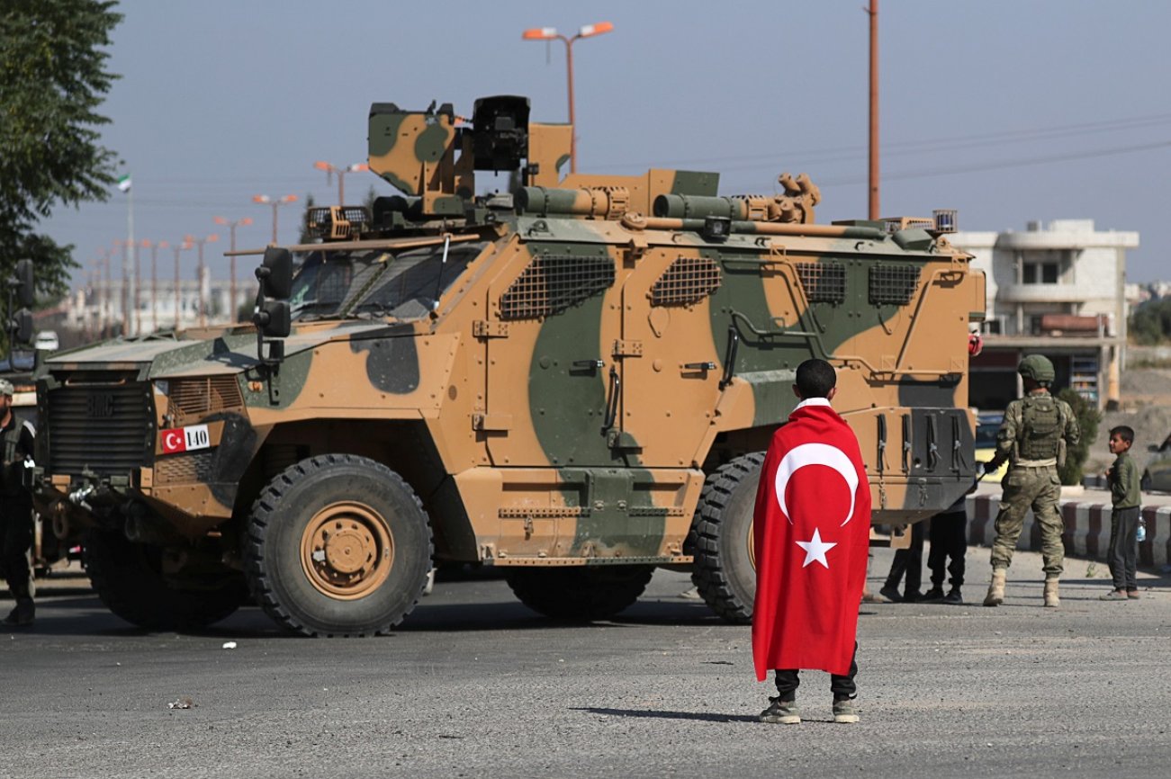 Boy wearing a Turkish flag stands in front of a Turkish military vehicle in the town of Tal Abyad